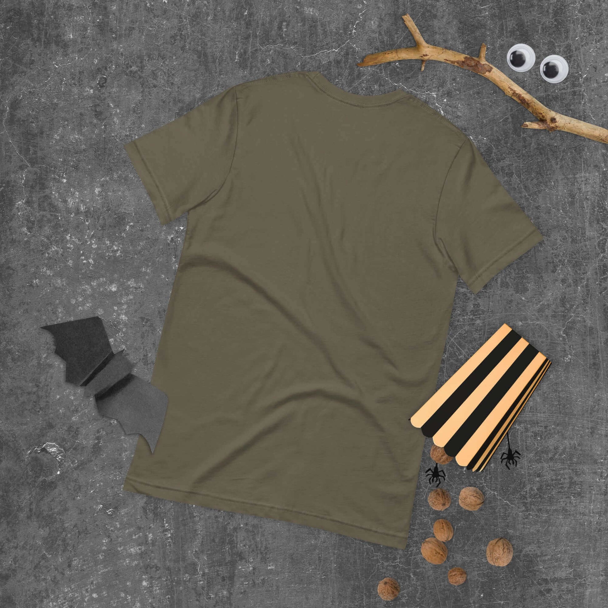 Back view of unisex t-shirt in olive green on a gray surface with Halloween decorations