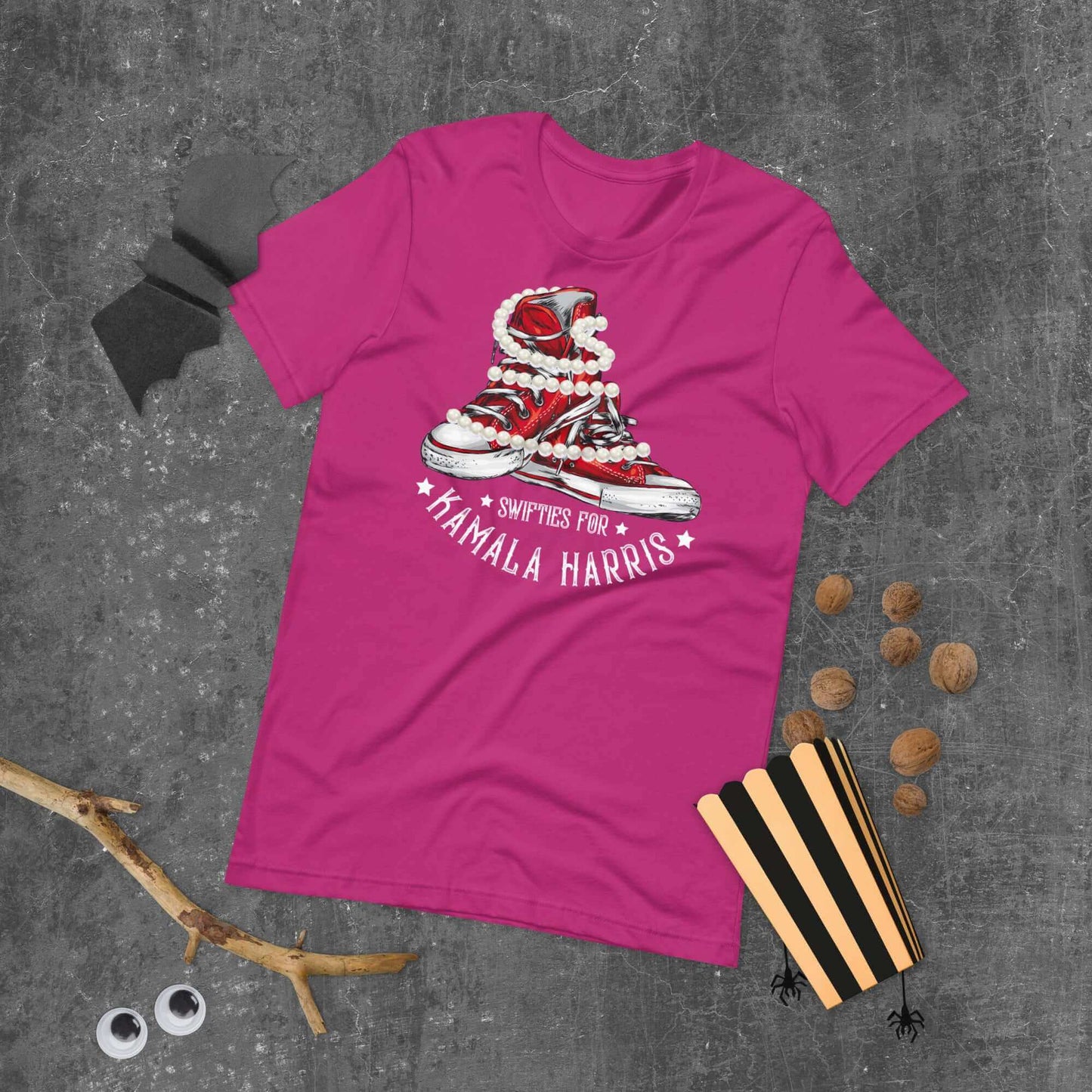 Pink t-shirt with Swifties for Kamala Harris Chucks and Pearls design on concrete background with Halloween accessories.