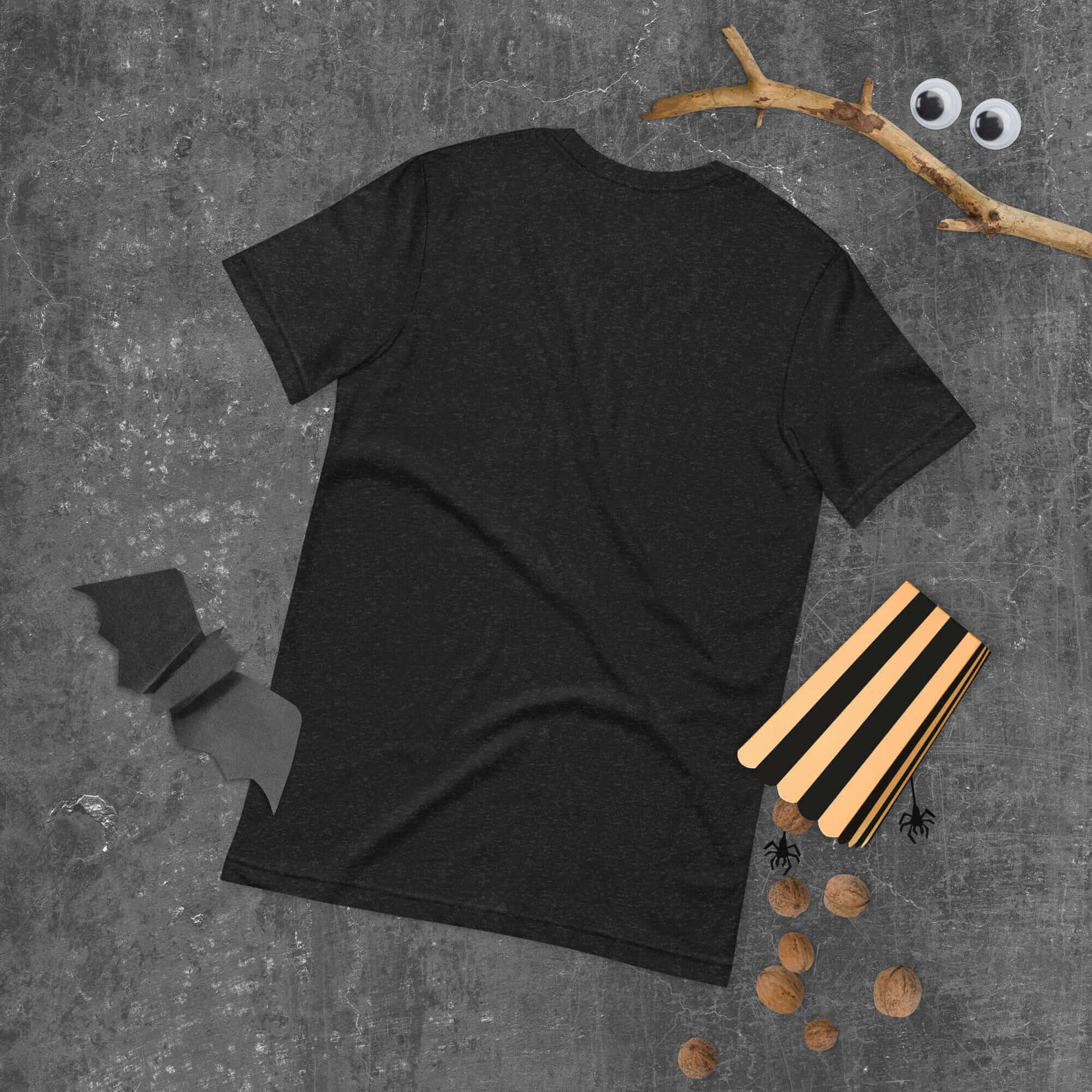 Black unisex t-shirt displayed on a textured surface with wooden craft sticks and decorative elements.