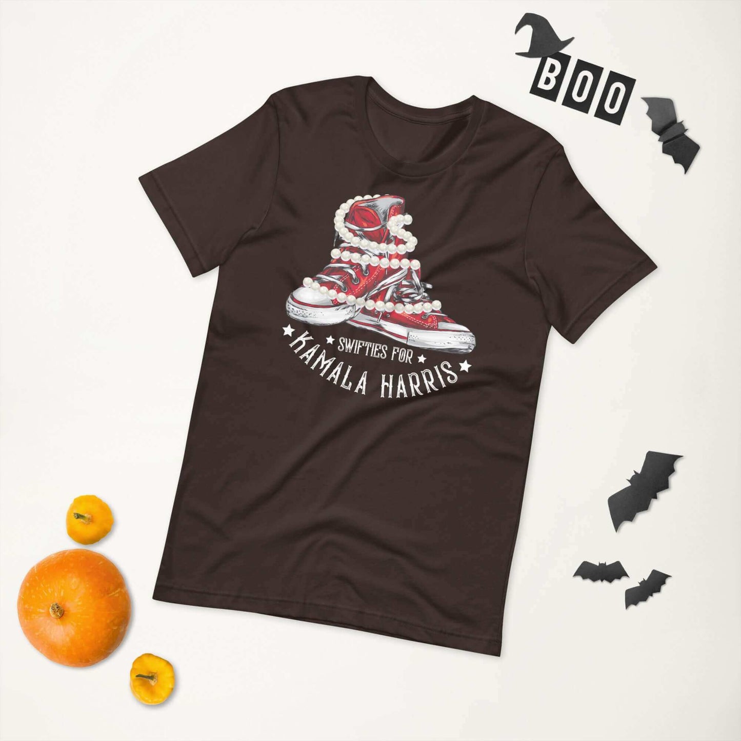 Unisex t-shirt with Swifties for Kamala Harris design, featuring chucks and pearls, laid flat with Halloween decorations.