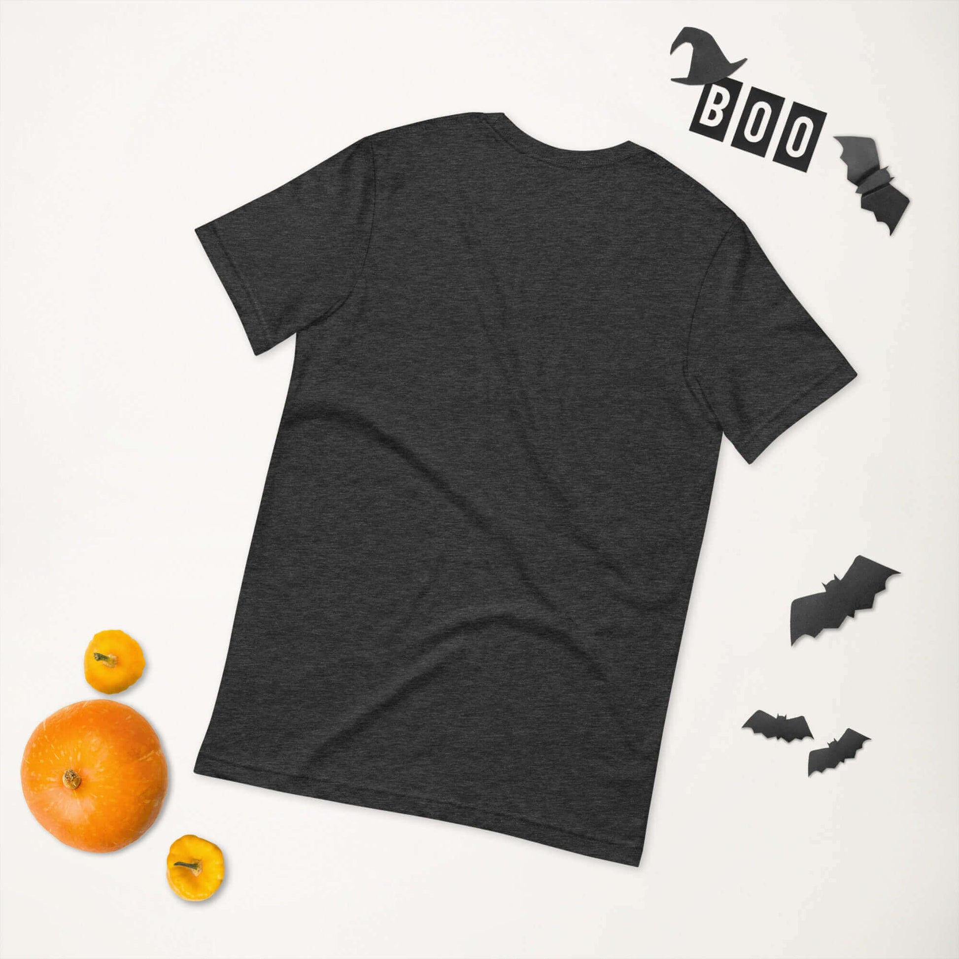 Dark gray unisex t-shirt displayed with Halloween-themed decorations and small pumpkins.