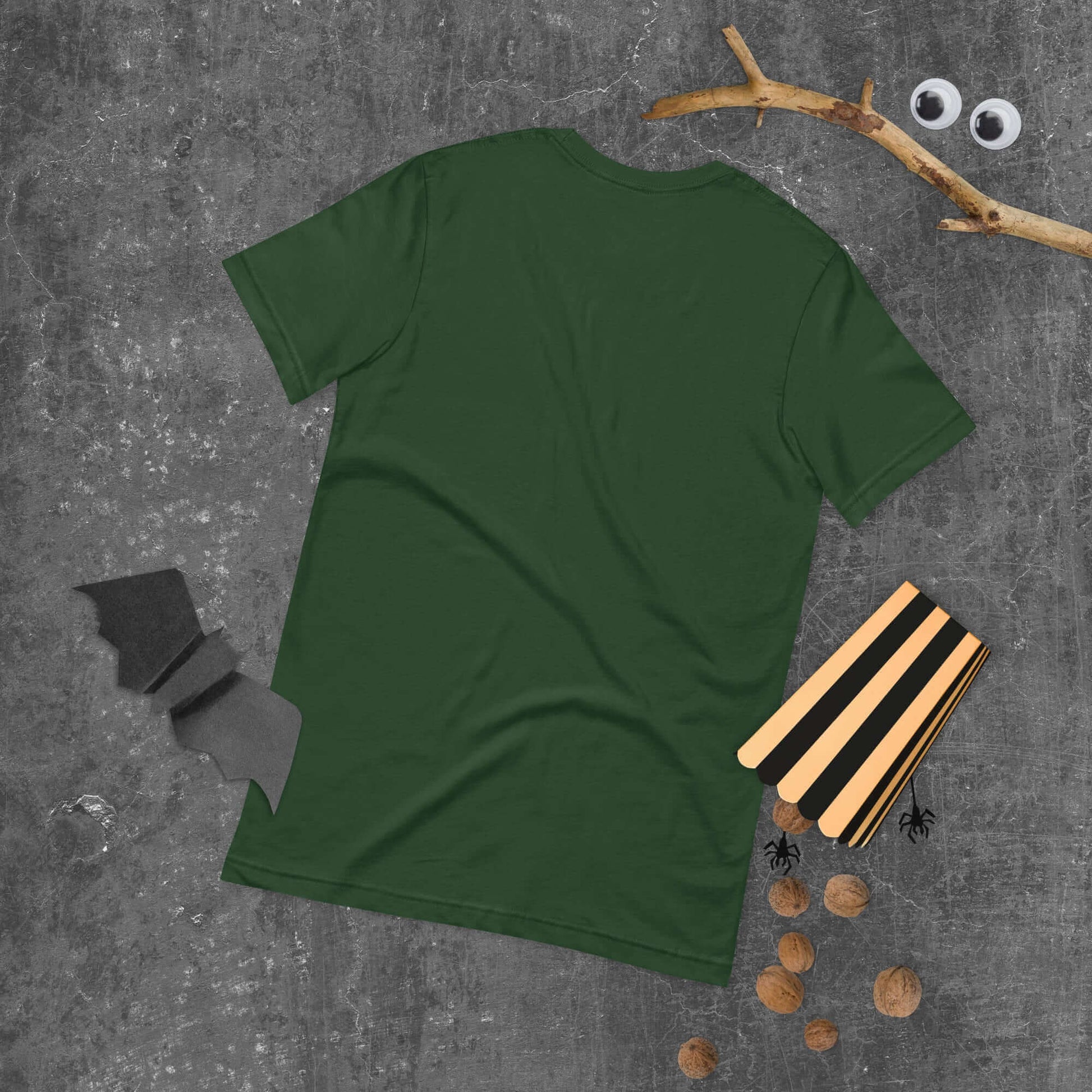 Green unisex t-shirt on gray background with Halloween-themed props including bat cutout and wooden blocks.