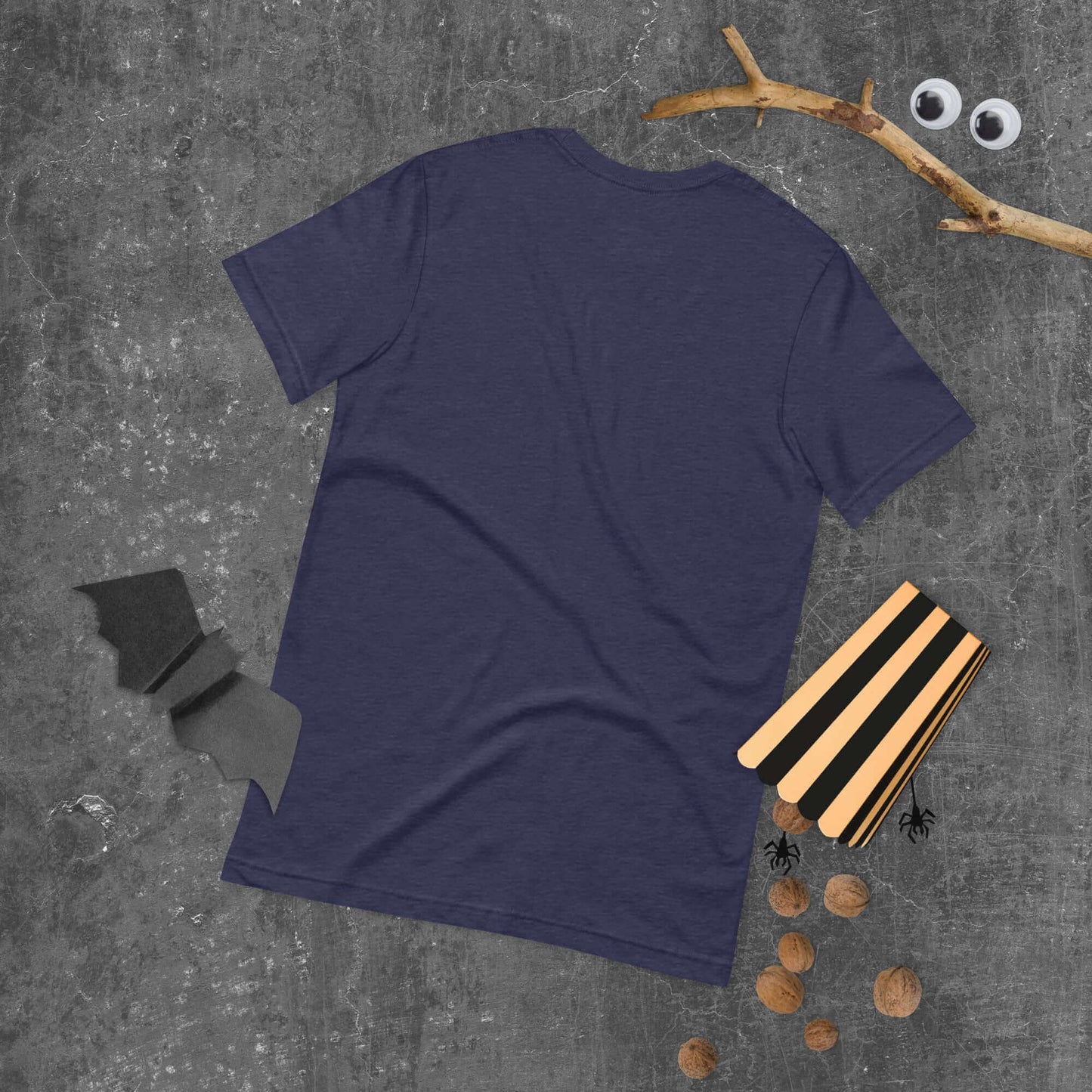 Back view of a navy unisex t-shirt on a textured surface with Halloween-themed props.