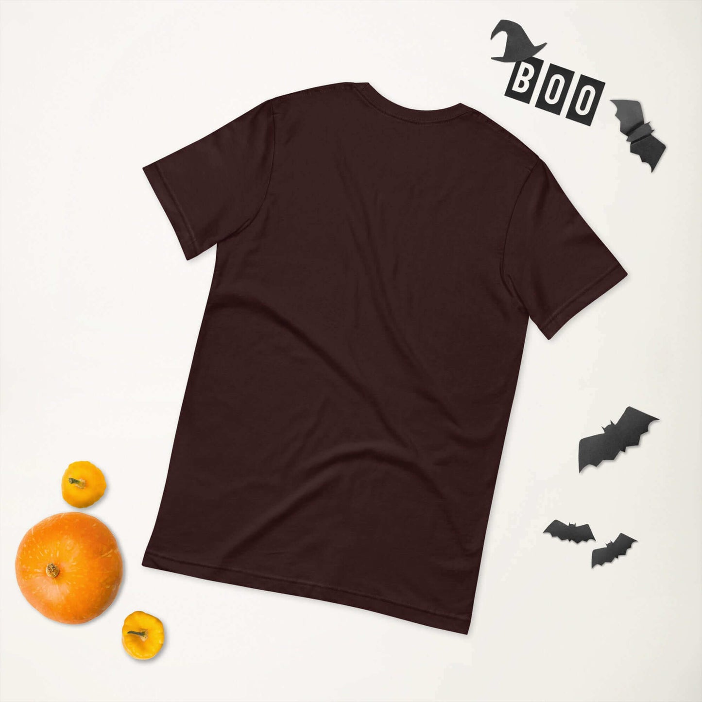 Dark brown t-shirt laid flat with Halloween theme decorations including bats, "Boo" letters, and pumpkins.