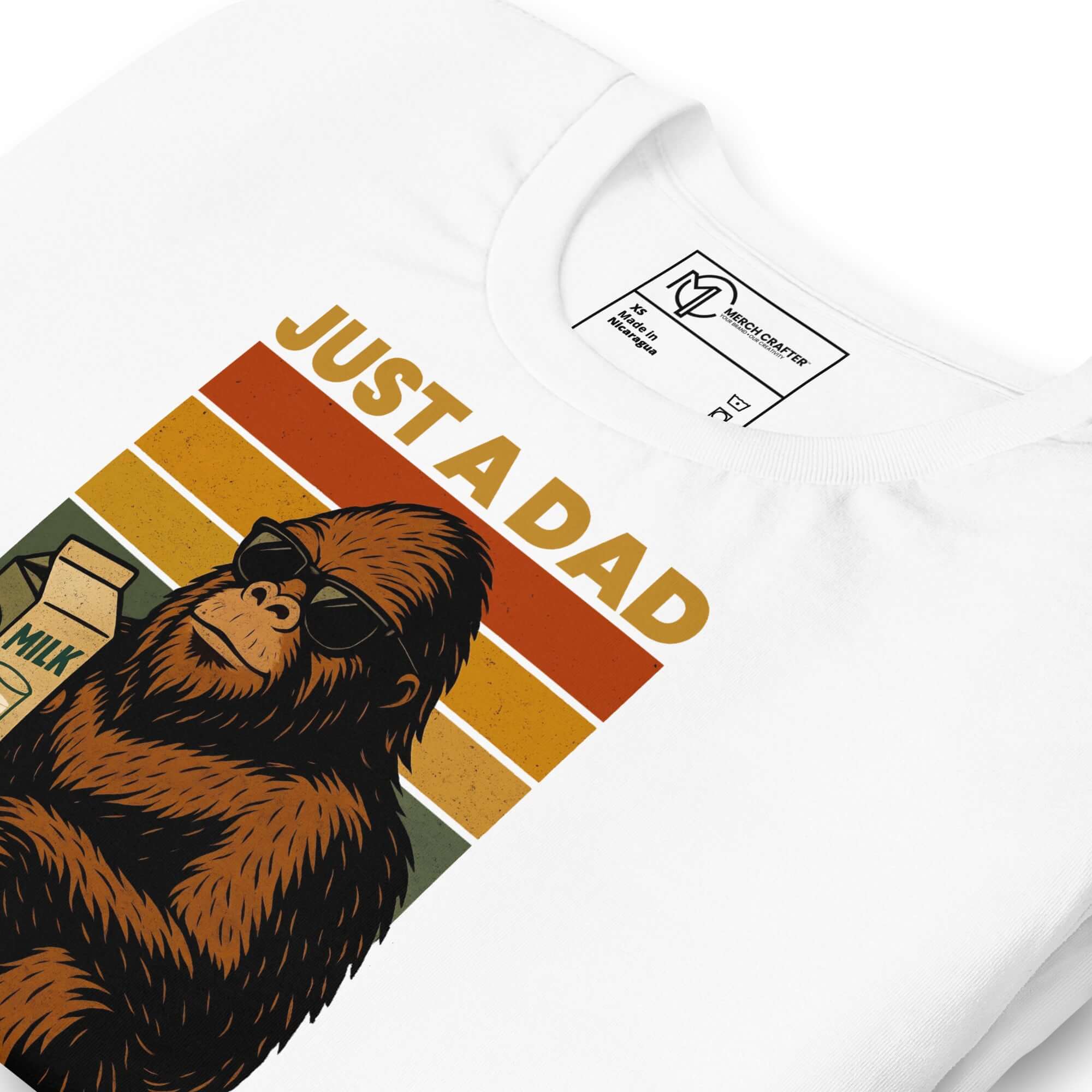 Just a Dad Bigfoot T-Shirt featuring a Sasquatch in sunglasses holding milk, with a retro stripe design.